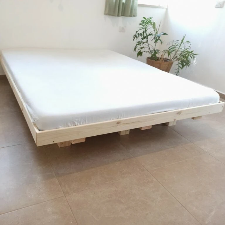 בסיס מיטה זוגית דגם "לילך" מעץ אורן עם מזרן לבן ועציץ ירוק ברקע