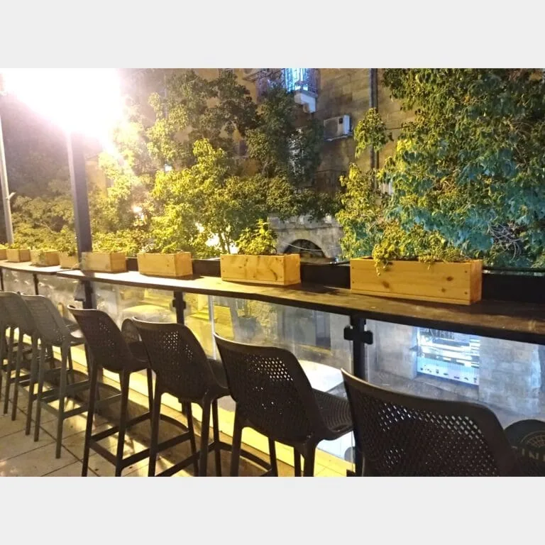 אדניות עץ דגם "איילת" שתולות צמחים על מעקה זכוכית במרפסת בר בלילה